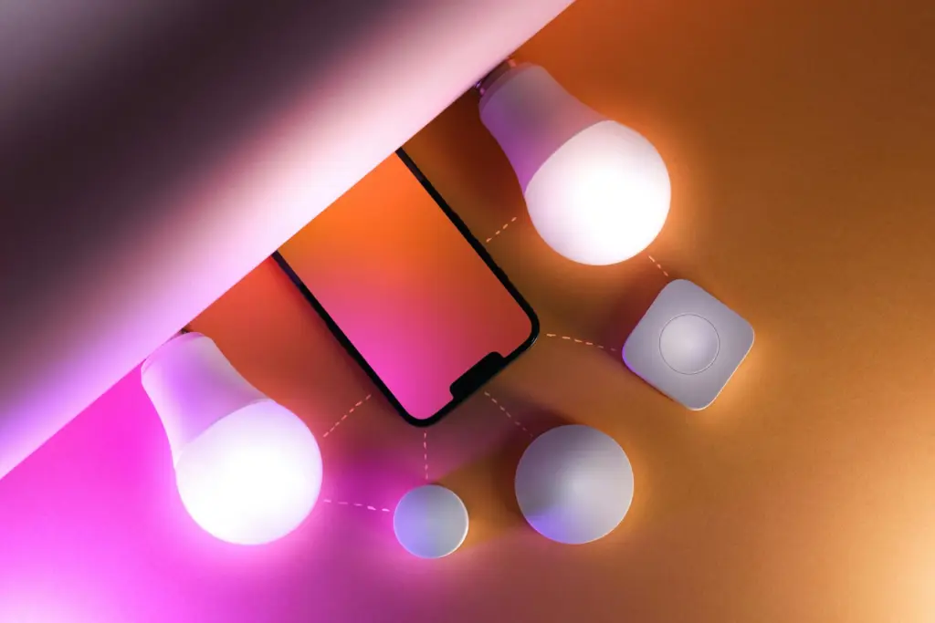 Stilvolle Komposition aus einem Smartphone mit farbigem Display, umgeben von leuchtenden smarten LED-Lampen und runden Smart-Home Sensoren, die über angedeutete Verbindungslinien miteinander vernetzt sind.